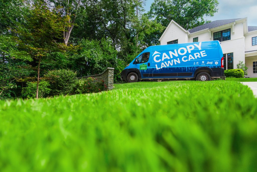 Canopy Lawn Care service van parked outside a home with a vibrant, healthy green lawn in the foreground